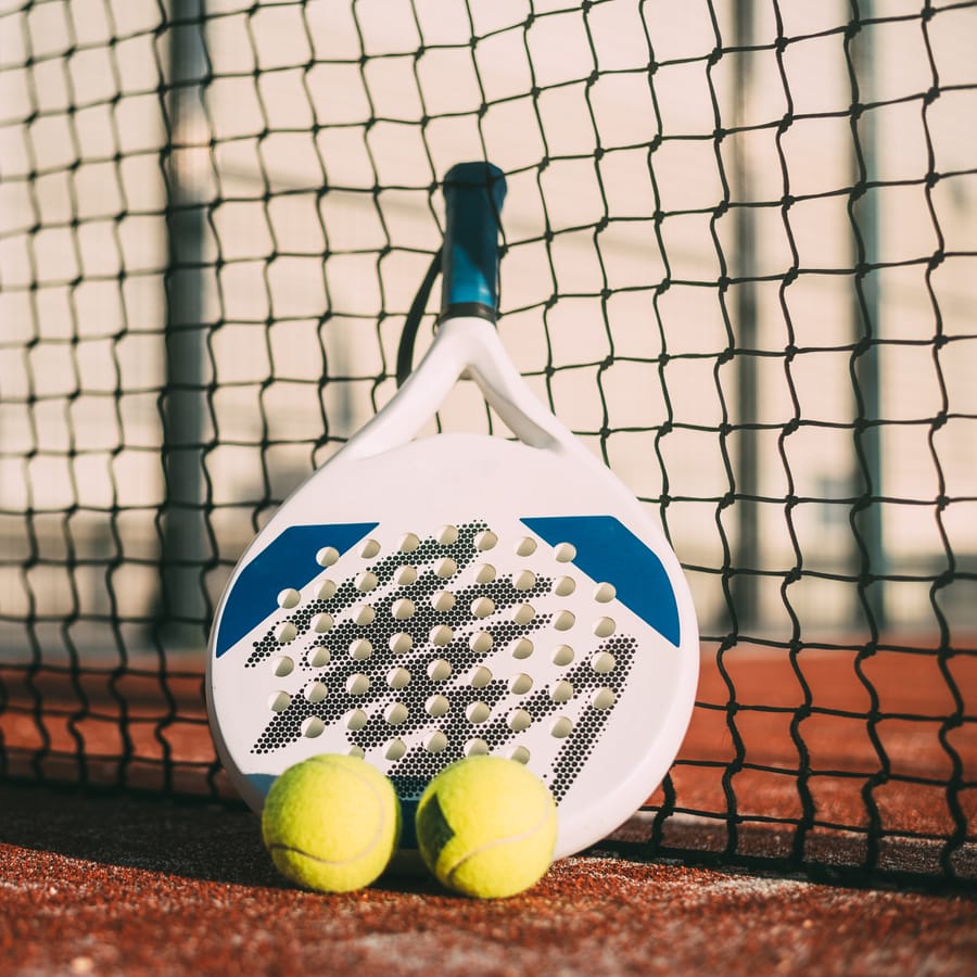 Racchetta da padel appoggiata alla rete con palline